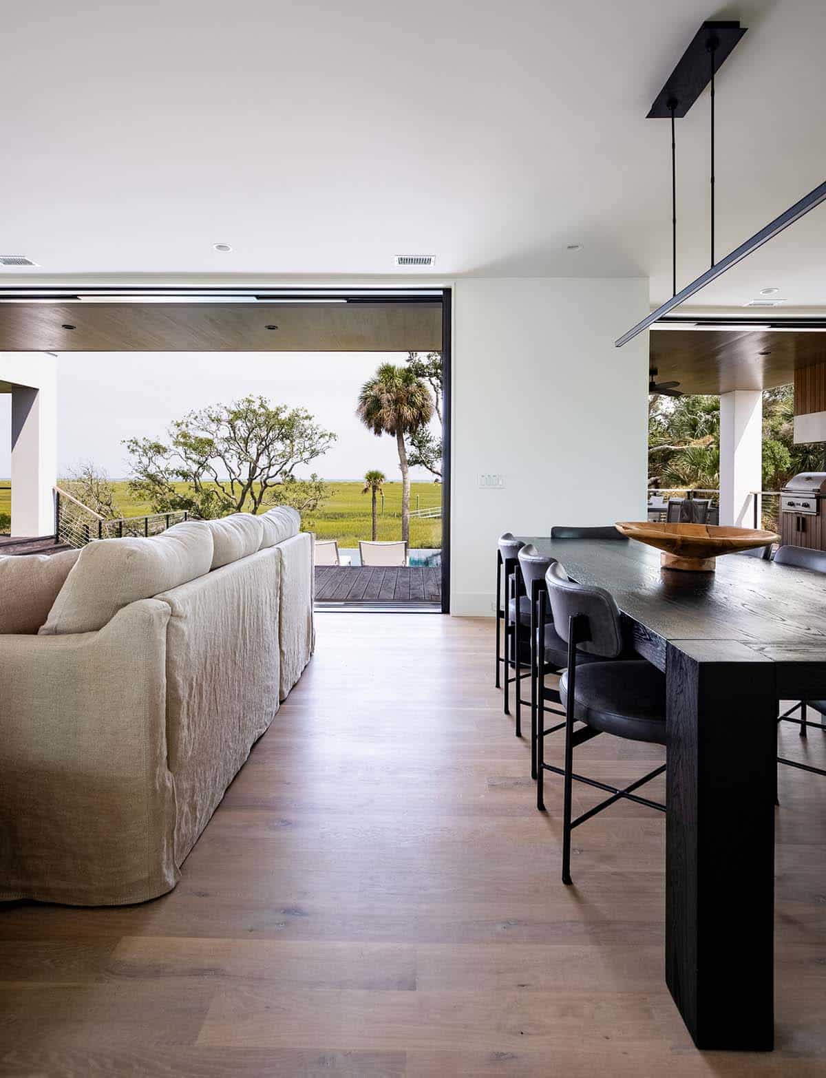 Living room with linen sofa and black dining table facing marsh view