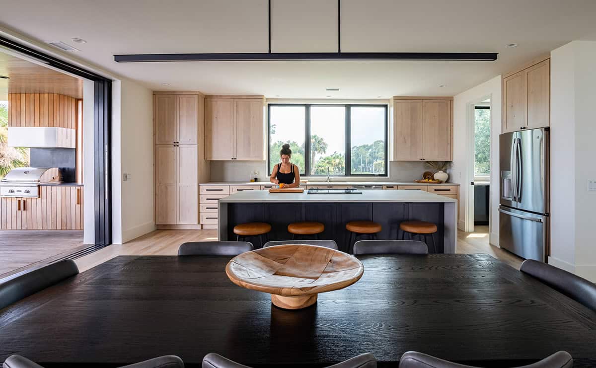 Kitchen and dining area with wood cabinetry and woman prepping food