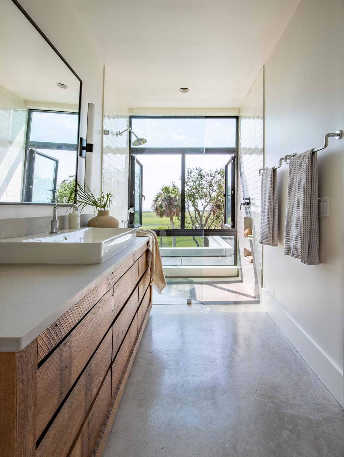 Bathroom with reclaimed wood vanity and glass shower opening to marsh view