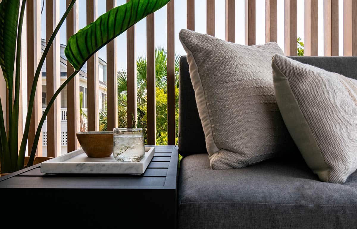 Outdoor side table with drink and bowl beside sofa pillows and slat screen