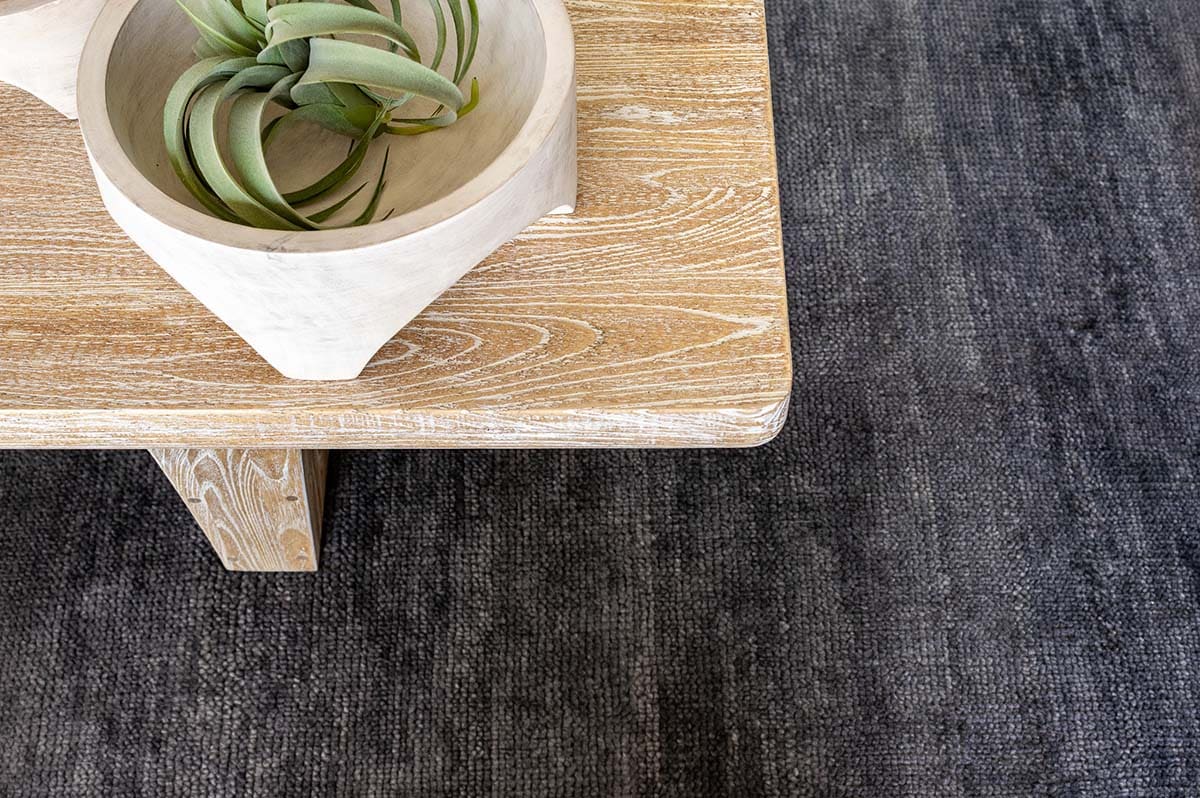 Close-up of wood coffee table with carved bowl and air plant on gray rug