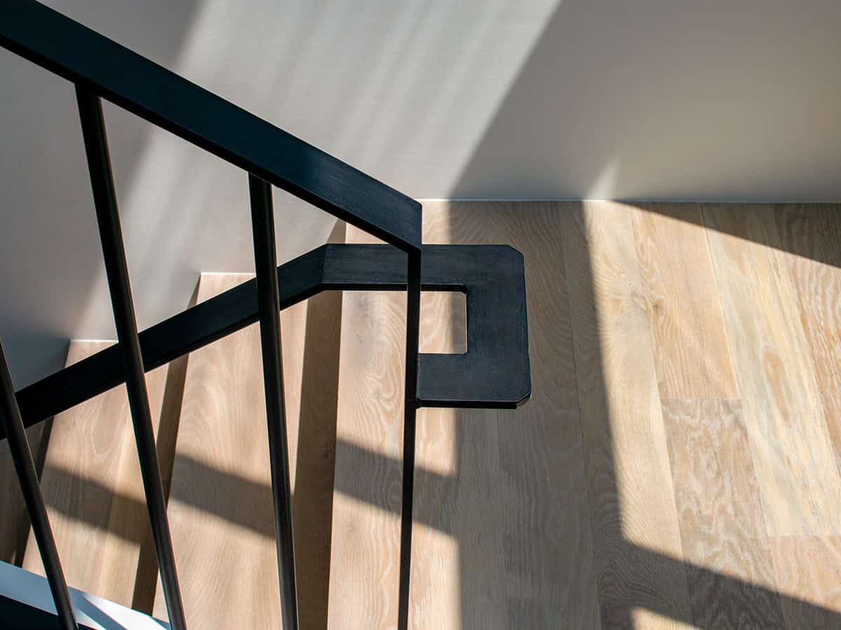 Detail of black metal stair railing casting shadows on wood floor