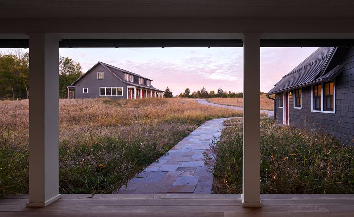 View from porch across meadow toward matching gray guest cottage with red door