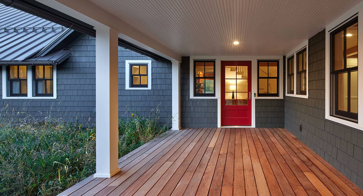 Covered wraparound porch with wood decking, white beadboard ceiling, and red front door