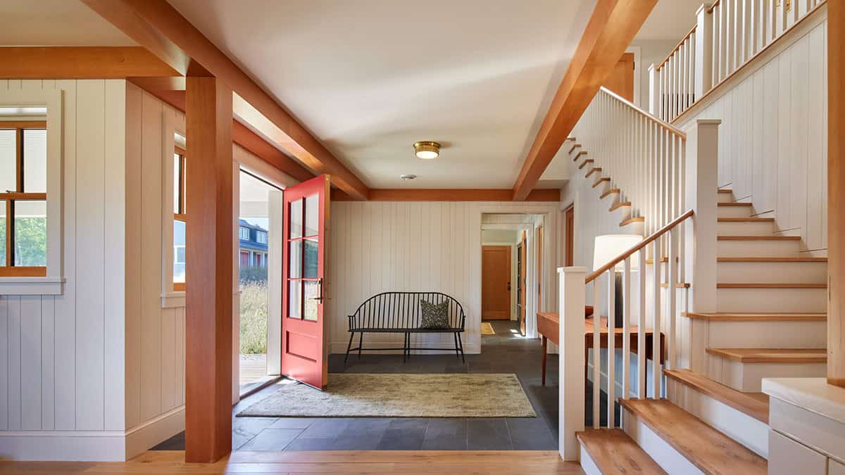 Bright entryway with red door, wood ceiling beams, white walls, and a staircase