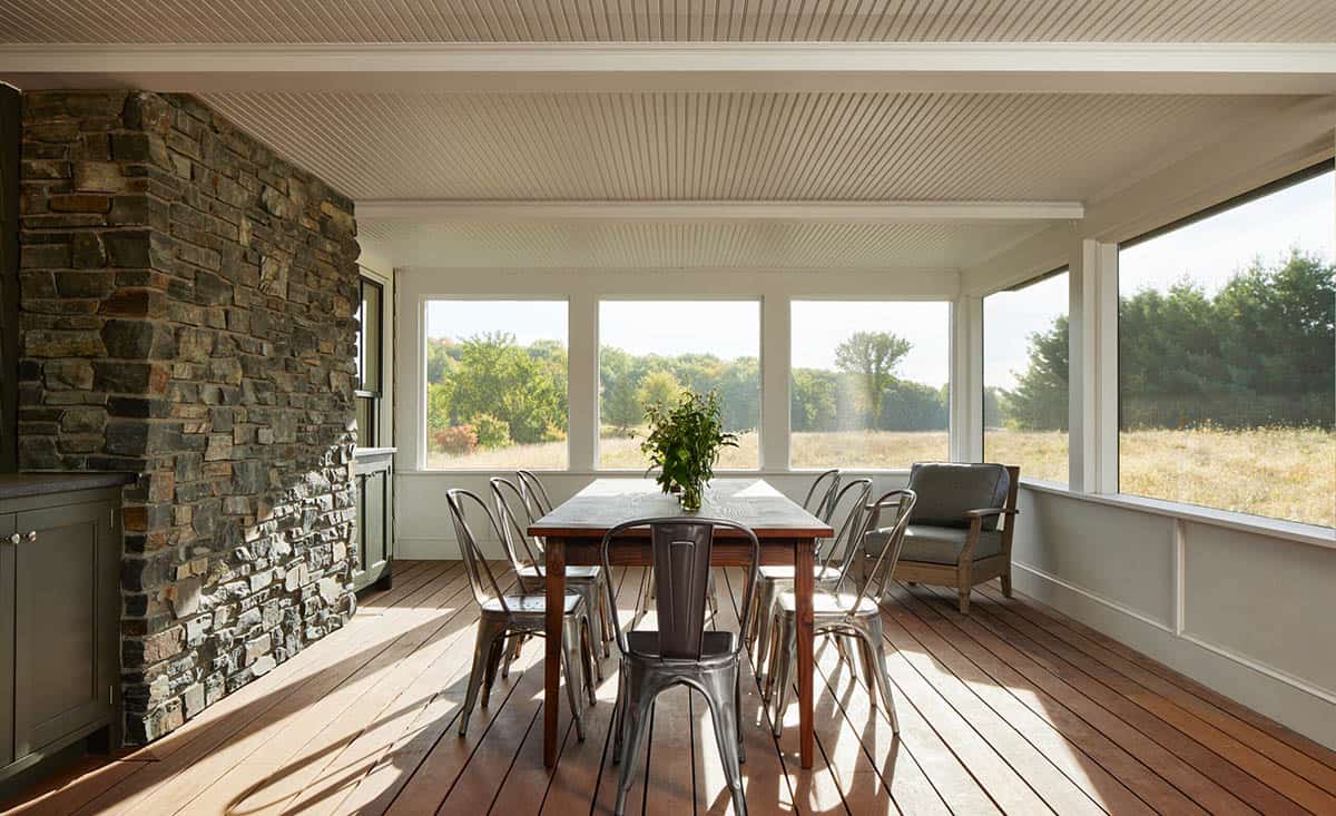 Screened porch with stone fireplace, wood dining table, and metal chairs