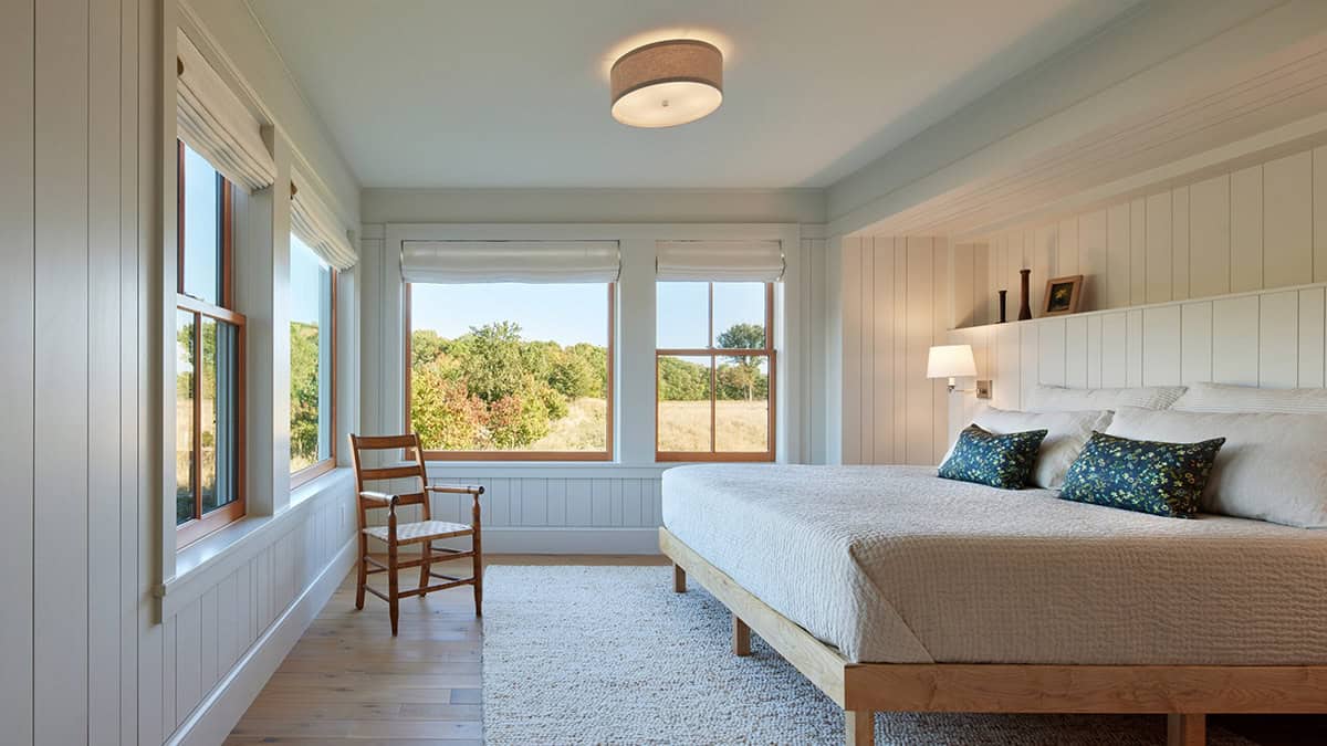 Bedroom with pale blue-gray paneled walls, wood bed frame, and meadow view