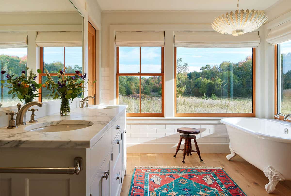 Bright bathroom with marble vanity, clawfoot tub, patterned rug, and brass chandelier
