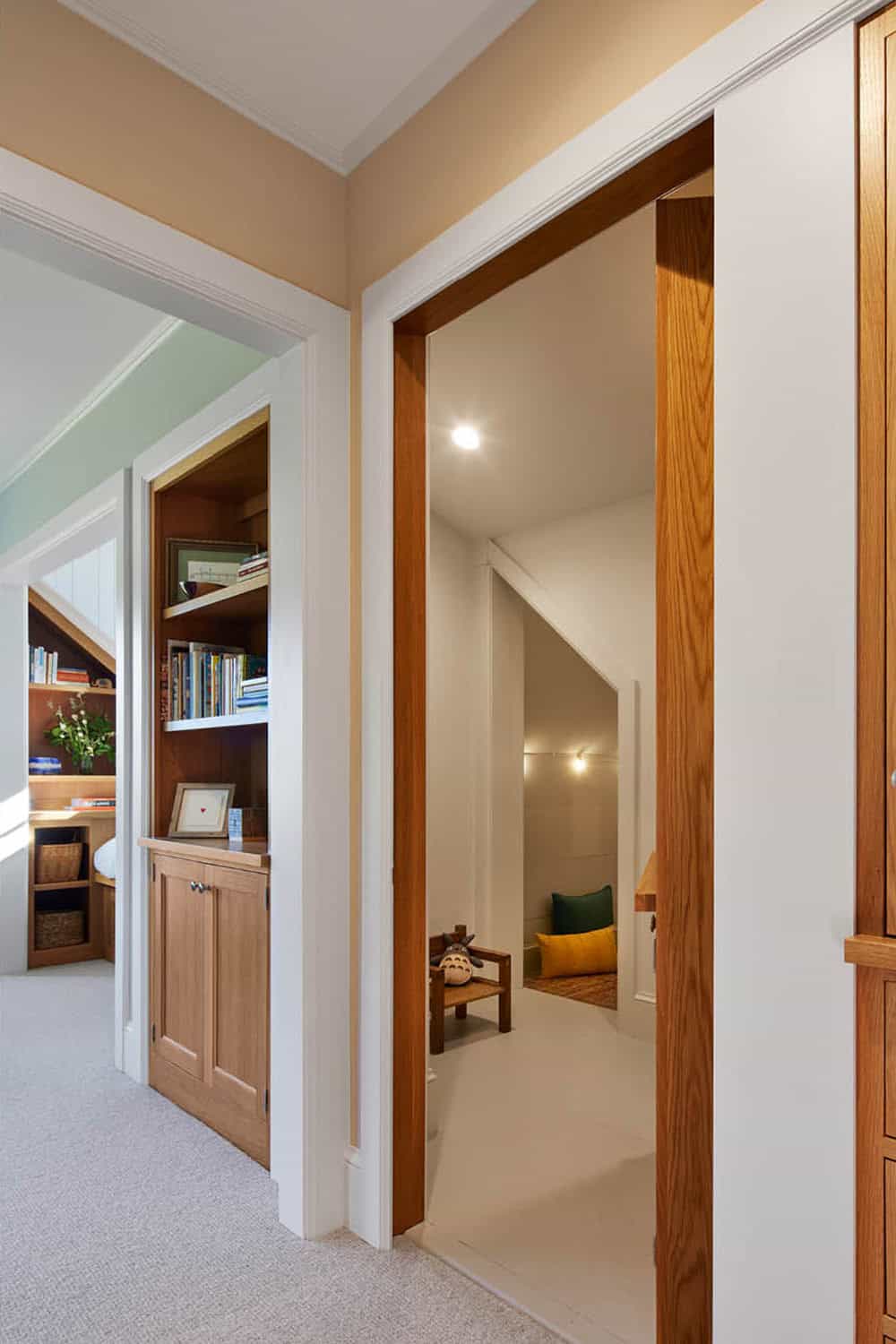 Hallway with bookshelves and open door revealing a cozy kids nook under the roofline