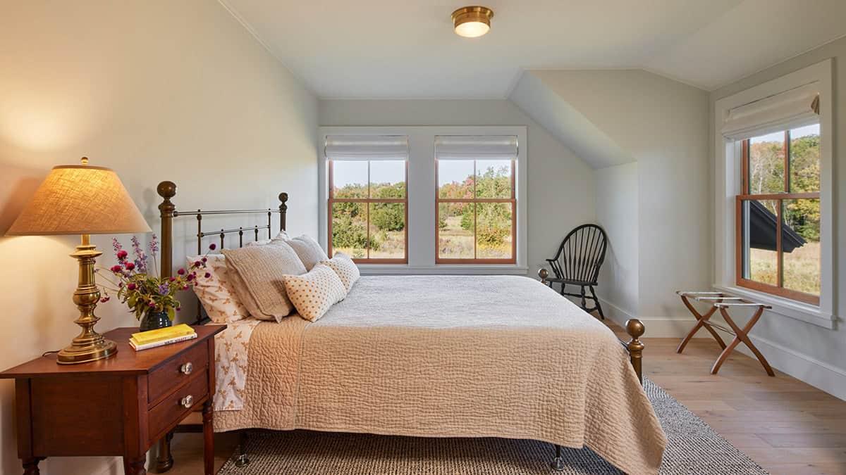 Guest bedroom under a sloped ceiling with brass bed frame and meadow view