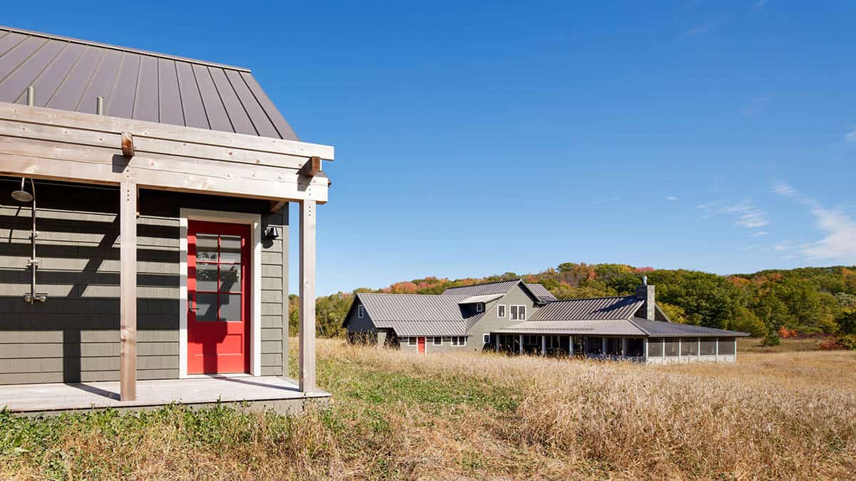 Exterior view across meadow with outdoor shower and main house complex in distance