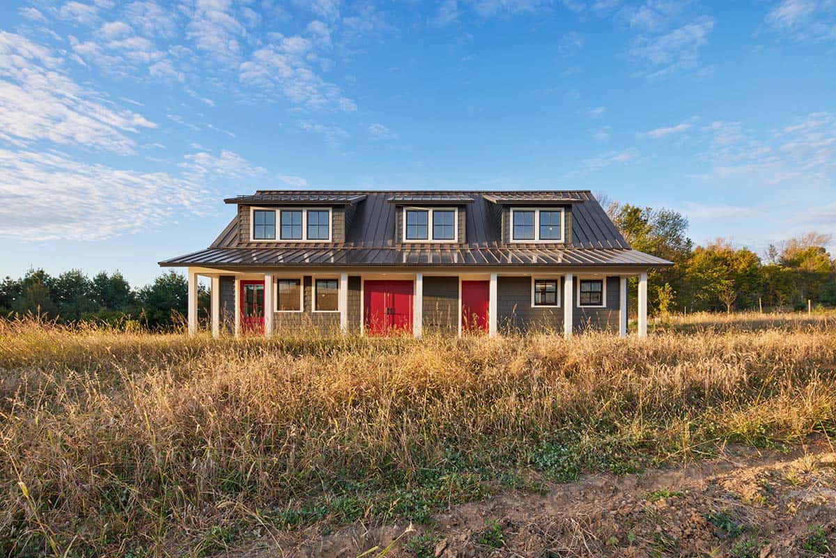Long single-story guest building with red doors and gambrel metal roof with dormers, in a golden meadow