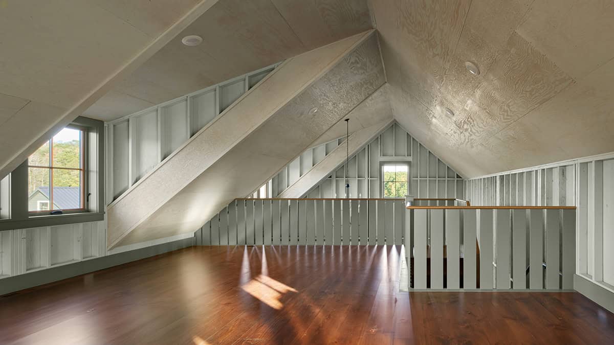 Unfinished attic loft with angled plywood ceiling, exposed studs, and wood floor