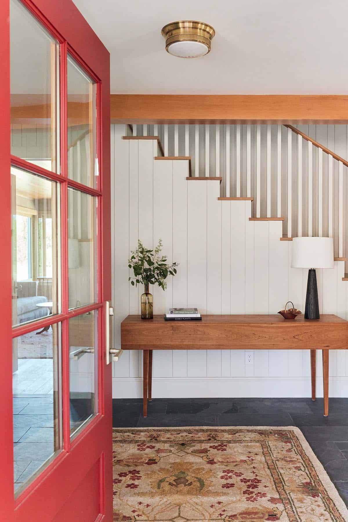 Entryway with red door, wood console table, floral rug, and slatted staircase