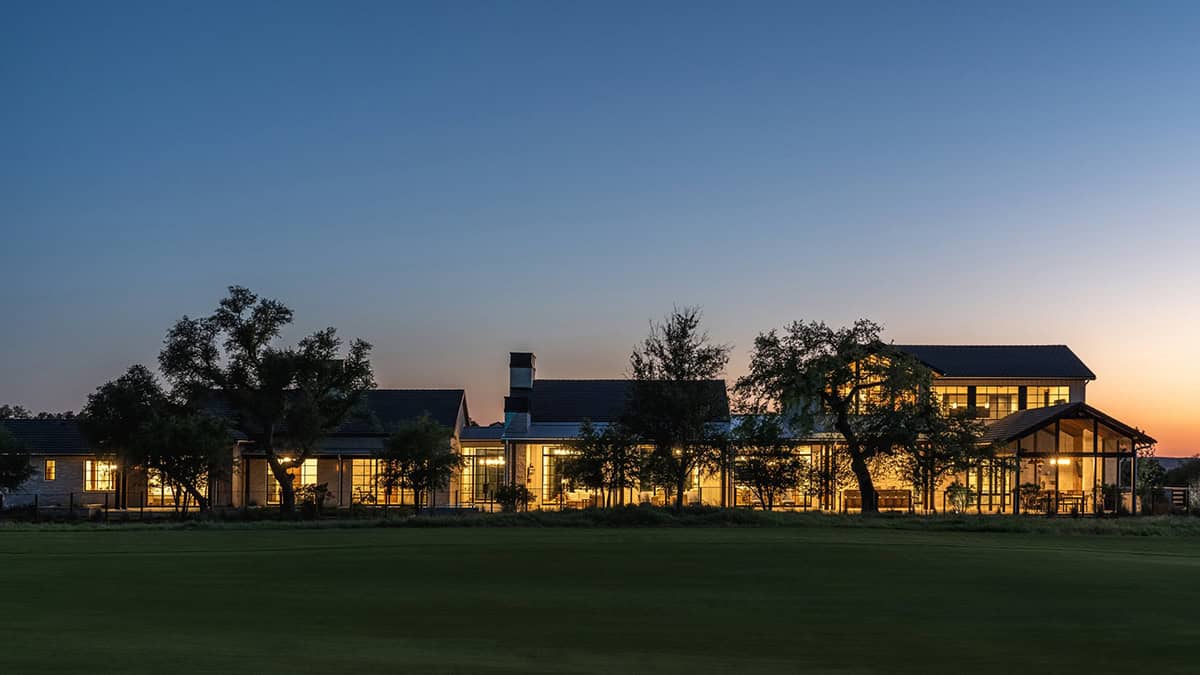 Sunset view of the ranch home glowing across the open lawn