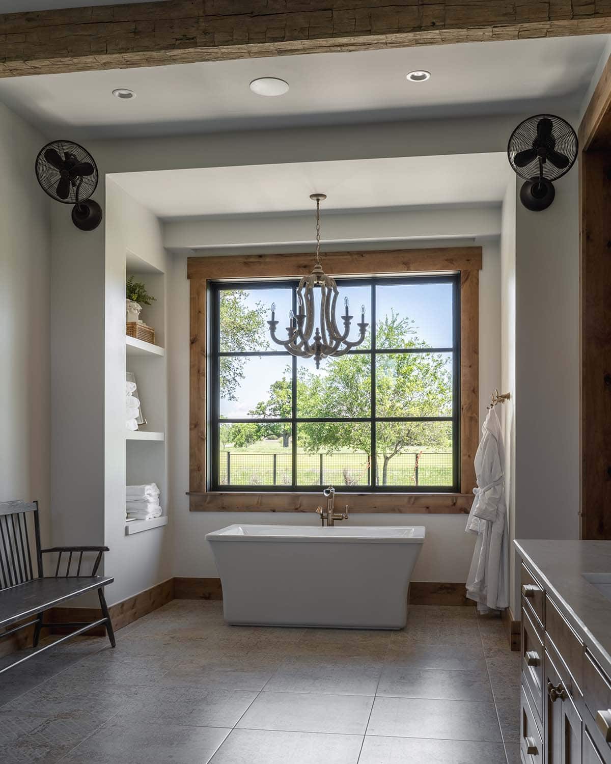Freestanding tub beneath a wood-framed window and wood-bead chandelier