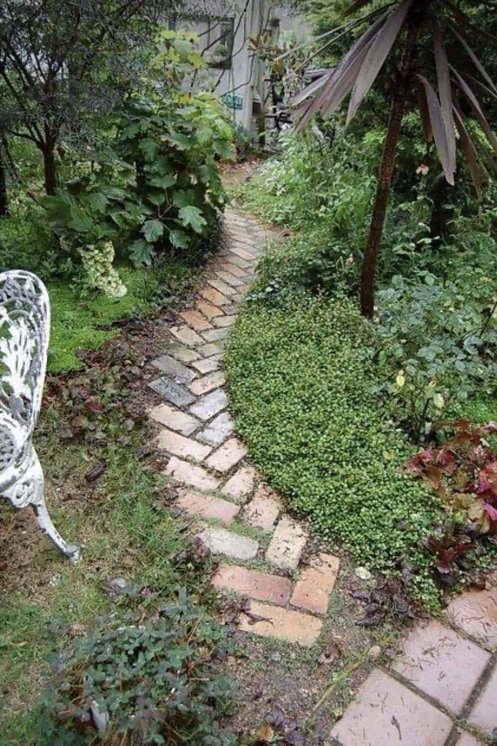 Herringbone brick garden path winding through lush green plantings