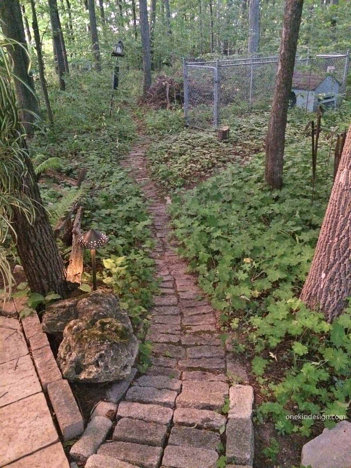 Narrow brick path winding through a wooded backyard in Ontario, Canada, leading to a fenced dog run