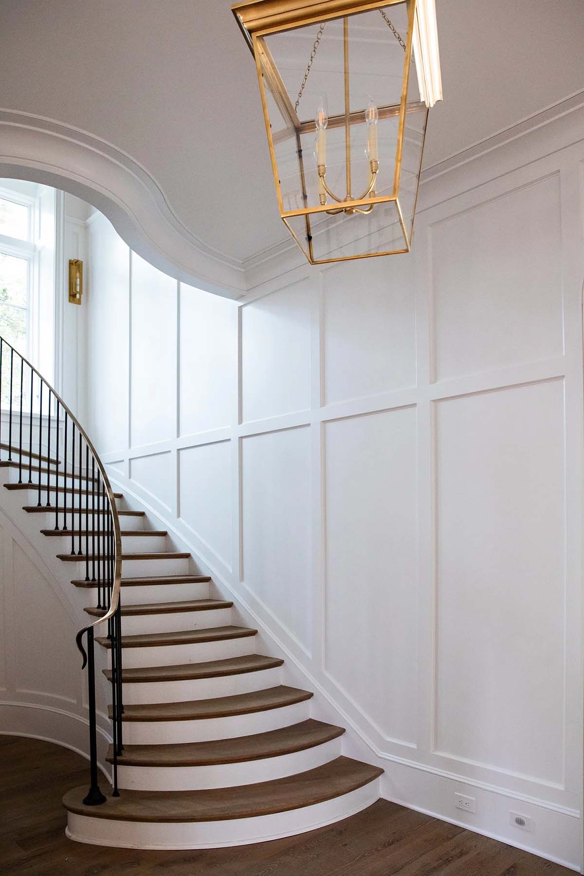 Curved staircase with wood treads, white wainscoting, and brass lantern pendant light