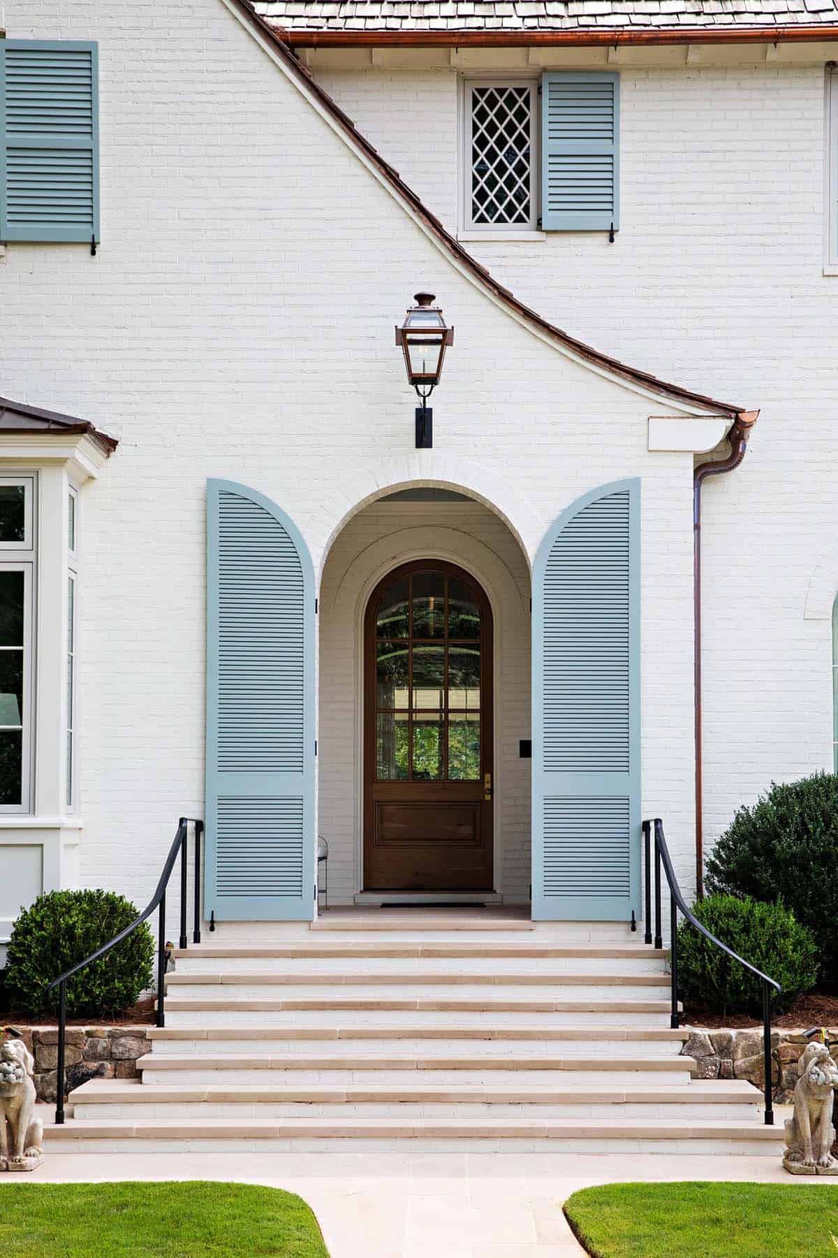 Arched front entrance with dusty blue louvered shutters and wood door, flanked by stone steps