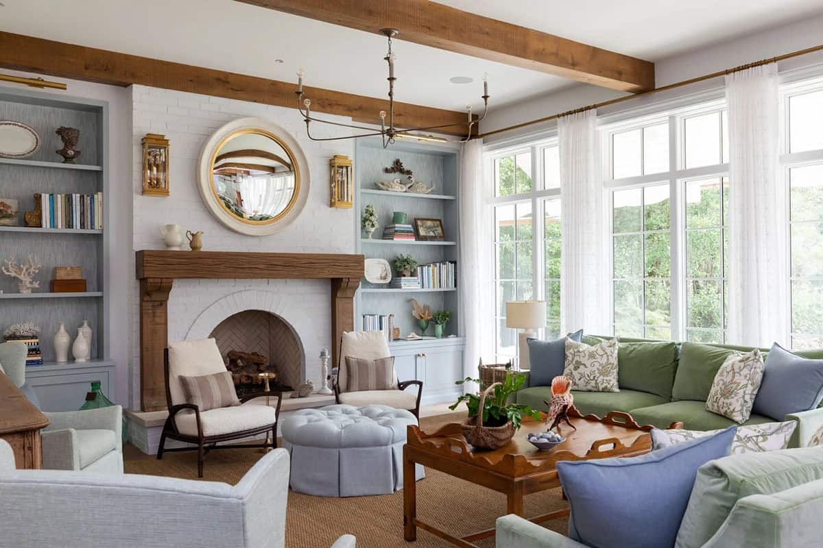 Living room with white brick fireplace, round mirror, green and blue sofas, and wall of windows