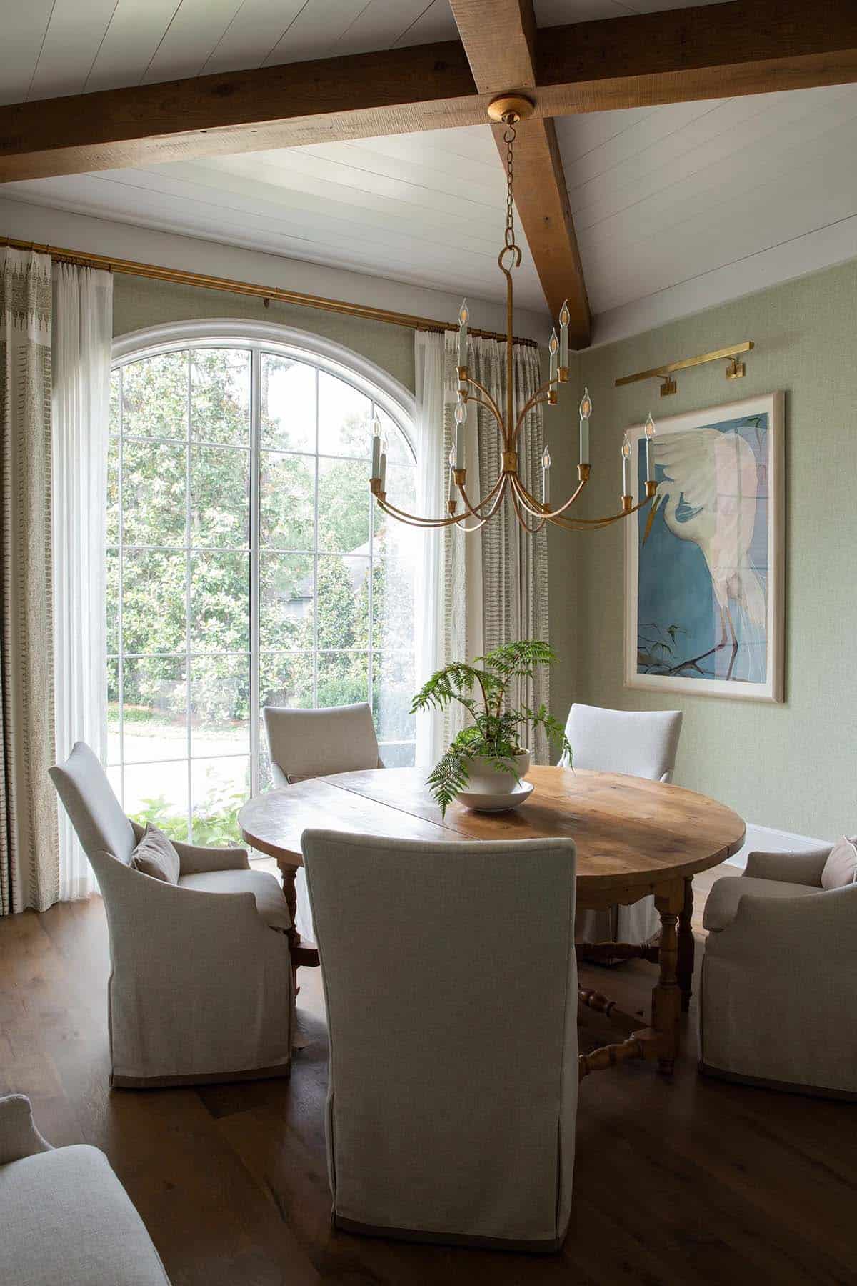 Breakfast room with round wood table, arched window, brass chandelier, and heron artwork