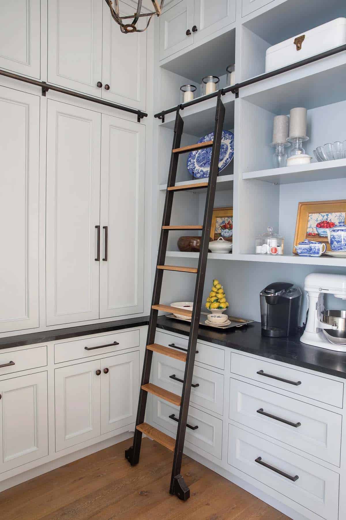 Pantry with black rolling ladder, light blue open shelving, and dark soapstone counter
