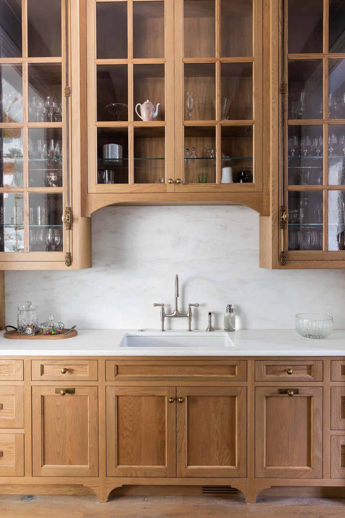 Butler's pantry with glass-front oak cabinets, marble backsplash, and bridge faucet