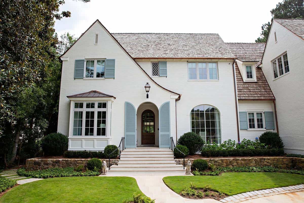 Front facade of white brick house with arched entry, blue shutters, and stone retaining wall