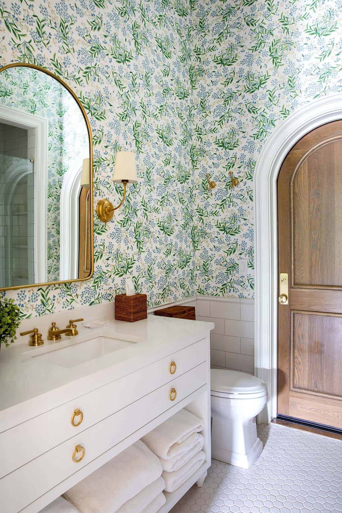 Powder room with floral wallpaper, brass fixtures, arched wood door, and hex tile floor