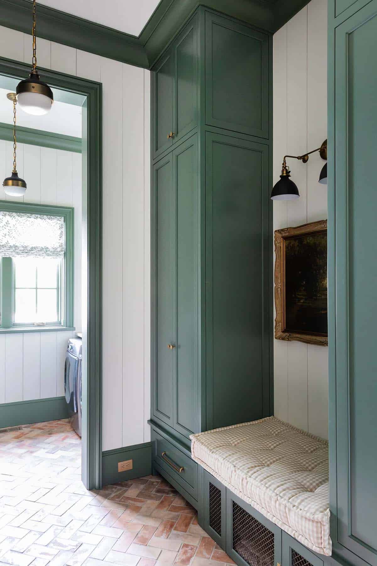 Mudroom nook with green built-in cabinetry, upholstered bench, and framed landscape painting