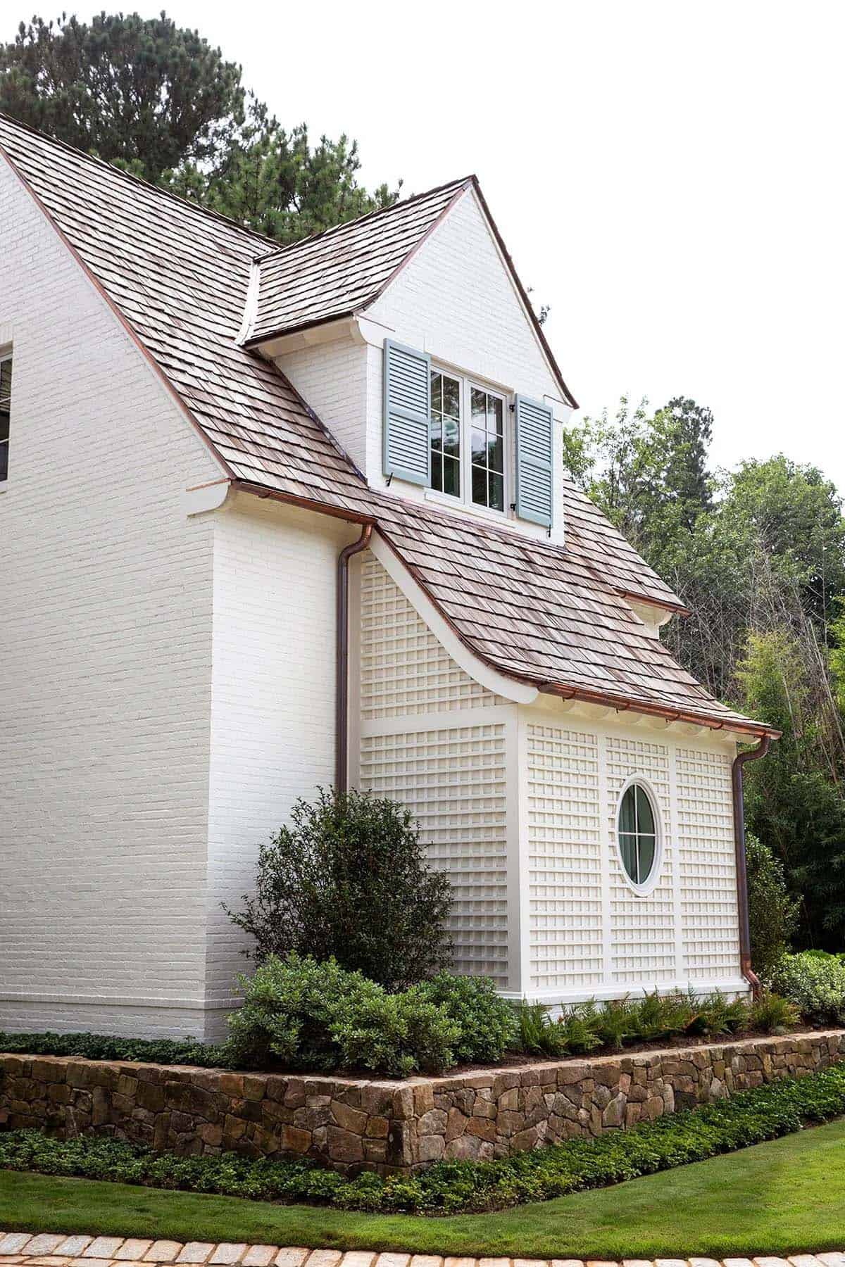 Exterior gable detail with lattice siding, oval window, cedar shake roof, and copper gutters