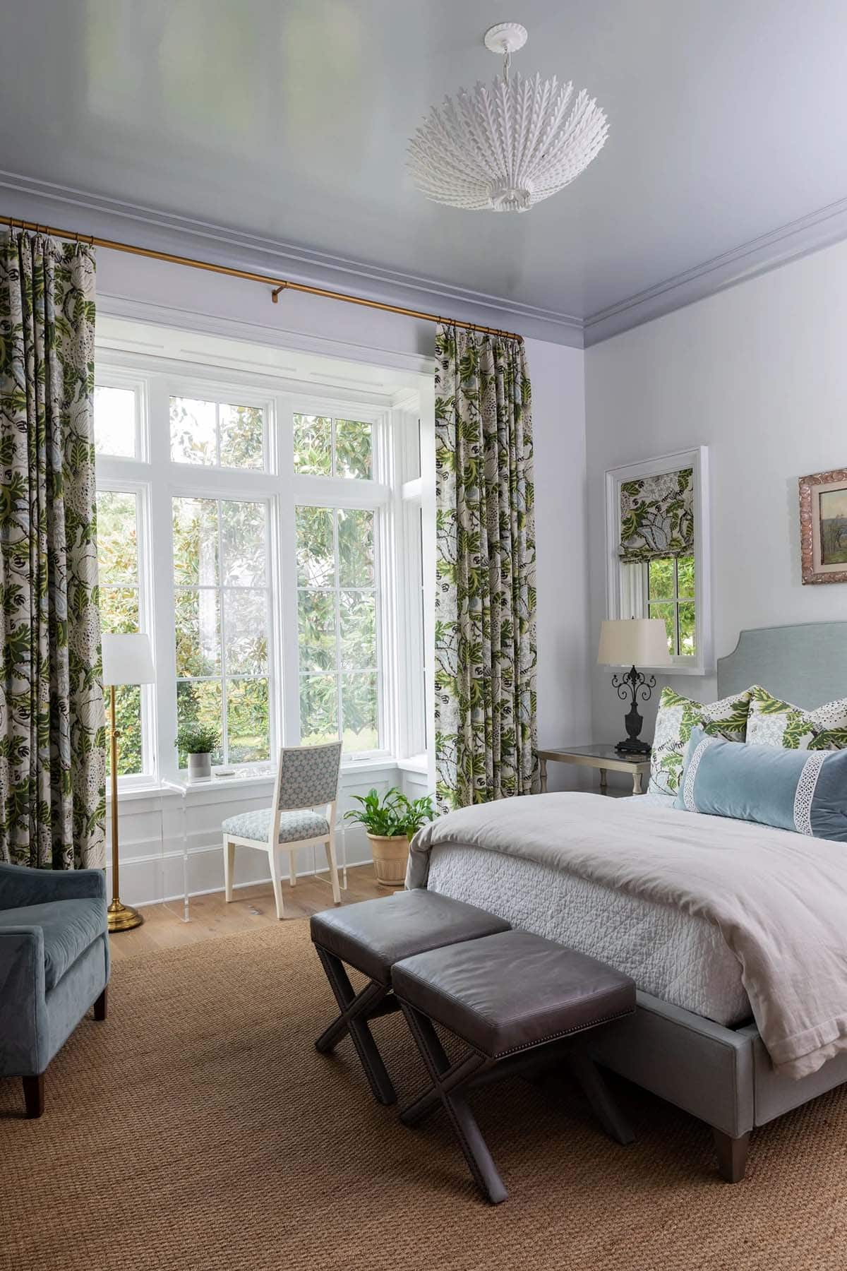 Primary bedroom with glossy blue ceiling, botanical print curtains, white coral chandelier, and blue upholstered bed