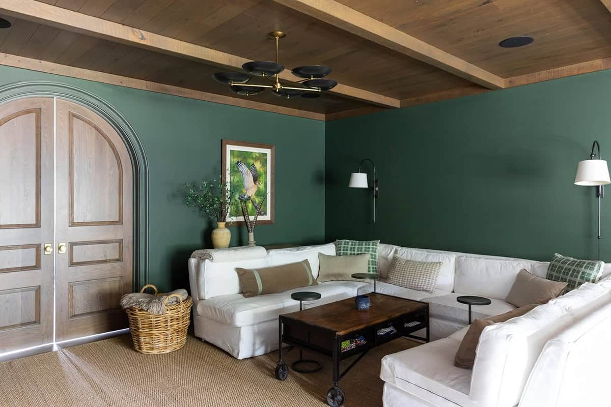 Game room with dark green walls, white sectional sofa, arched wood doors, and beamed wood ceiling