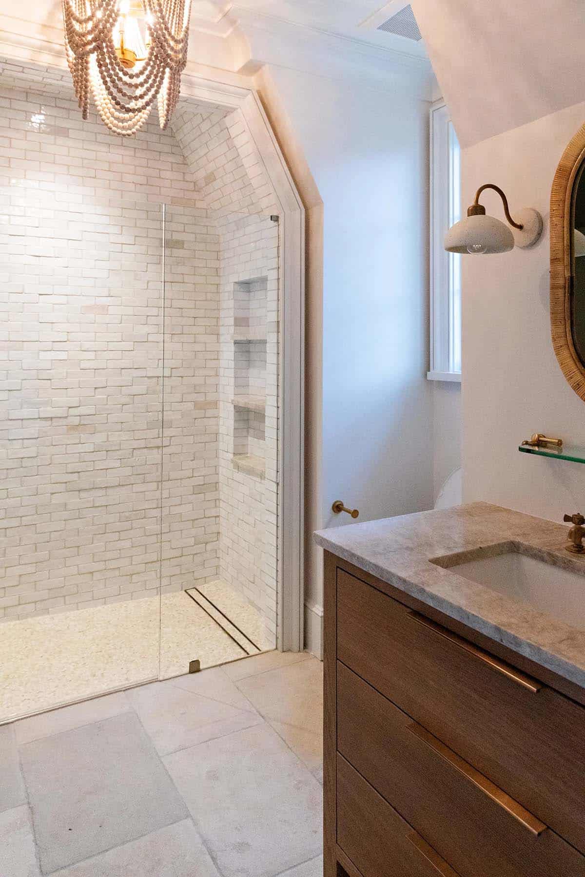 Bathroom with white brick-tile walk-in shower, bead chandelier, and dark wood vanity with marble top