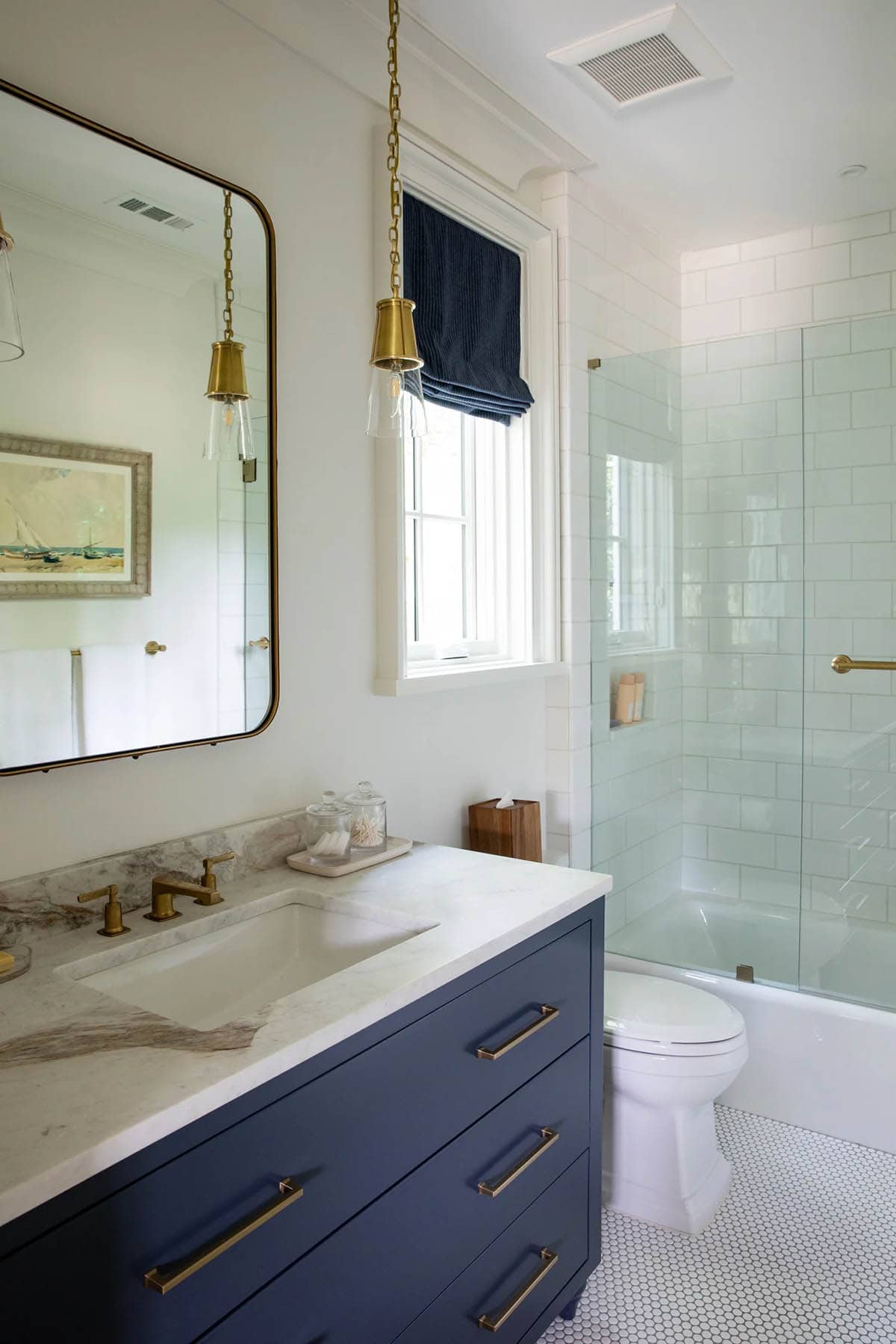 Bathroom with navy vanity, brass fixtures, glass pendant lights, and glass-enclosed shower