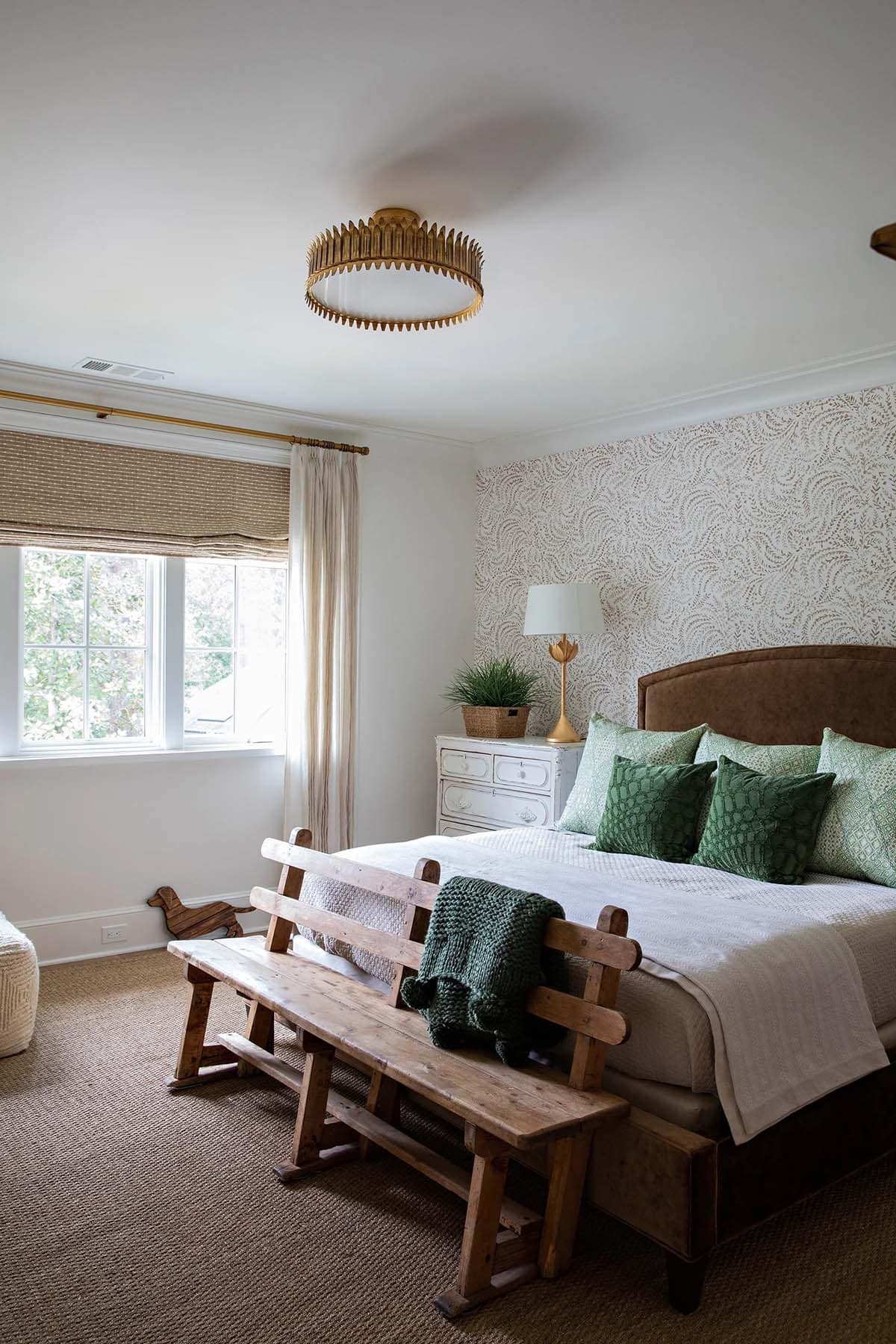 Bedroom with fern-patterned wallpaper accent wall, leather headboard, green pillows, and rustic wood bench