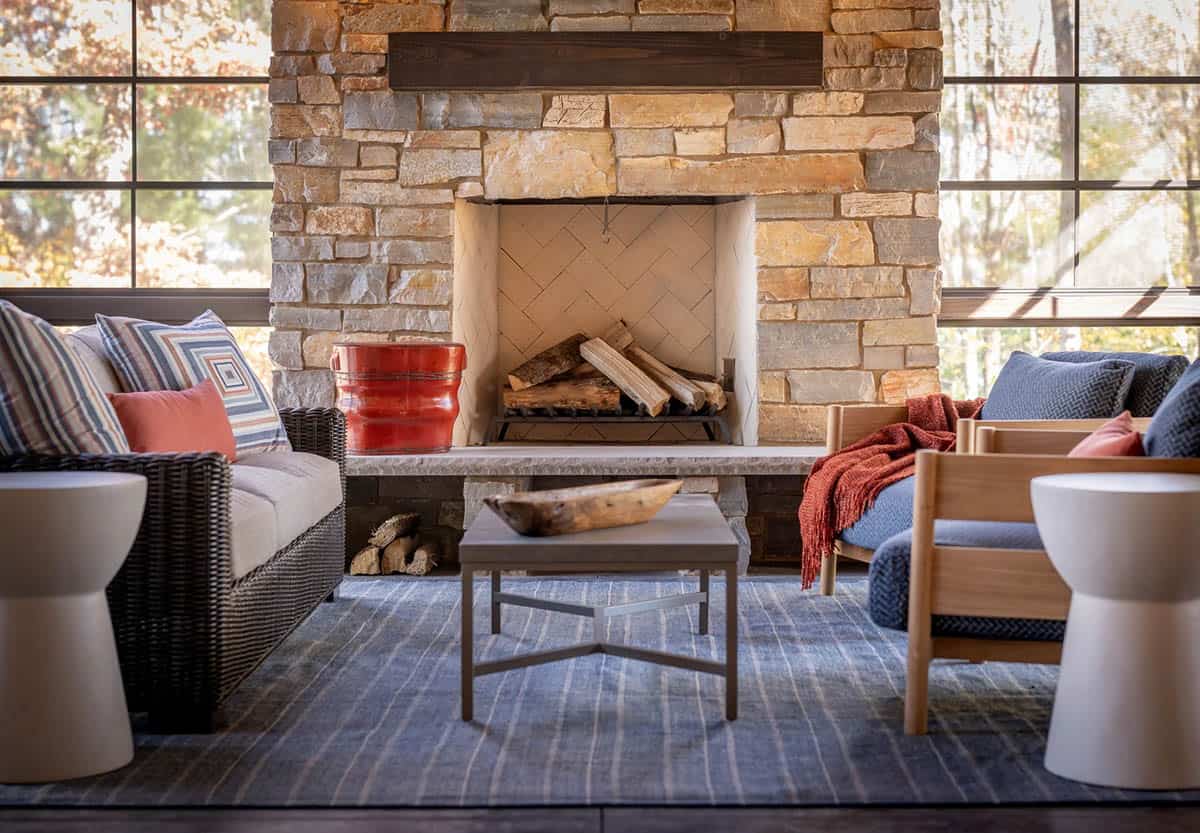 Close-up of stacked stone fireplace with wood mantel, herringbone tile firebox, and striped blue rug