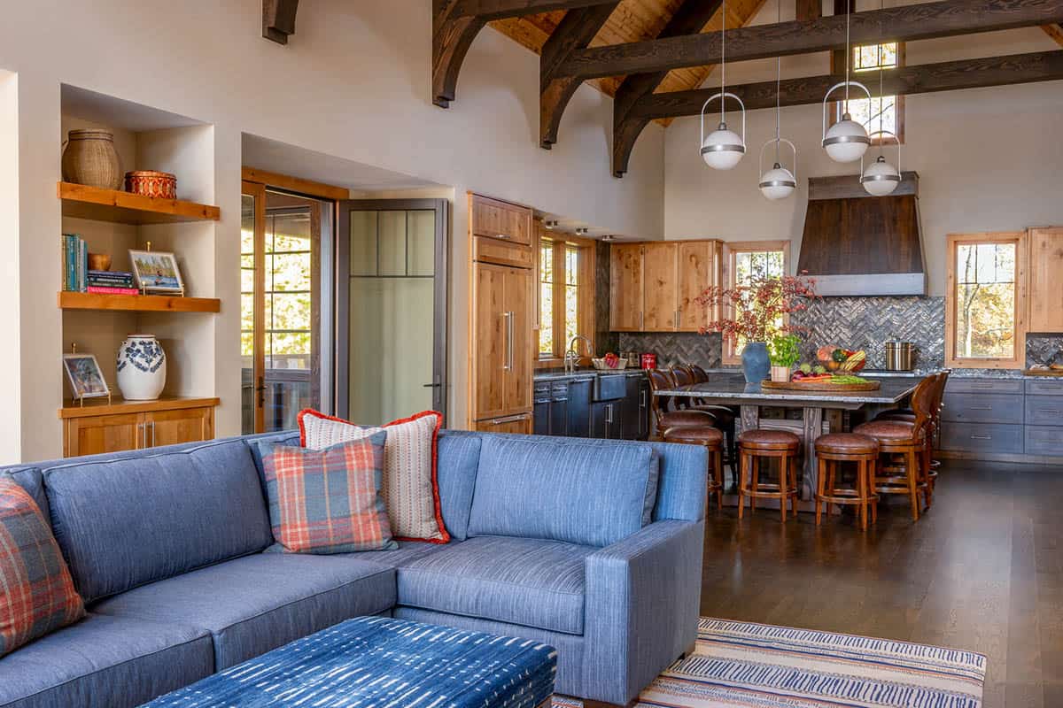 Open-concept living area with blue sectional sofa leading into a rustic kitchen with dark wood range hood