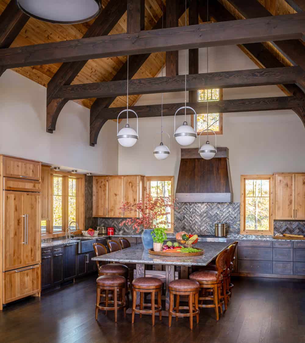 Vaulted kitchen with exposed timber trusses, globe pendant lights, and a large granite-topped island with leather stools