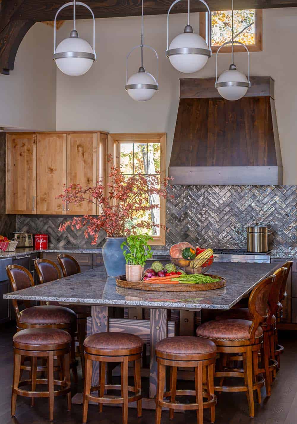 Kitchen island with granite top, leather barstools, globe pendant lights, and dark wood vent hood