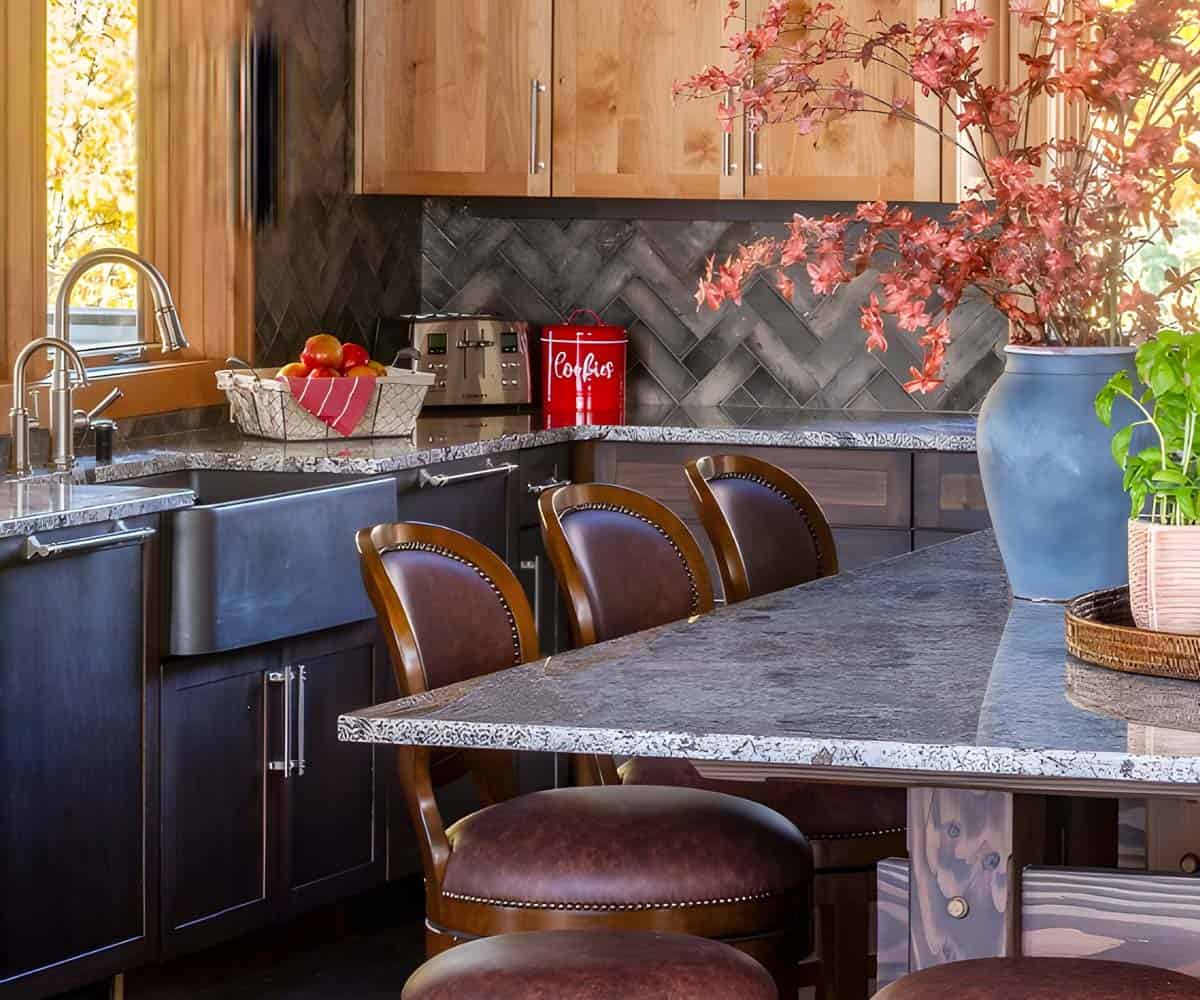 Kitchen corner with farmhouse sink, wood cabinetry, herringbone tile backsplash, and red accent decor