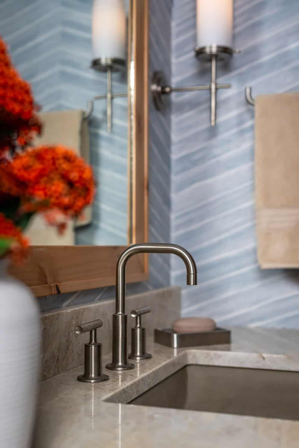 Close-up of bathroom faucet and sconces against blue chevron-striped wallpaper