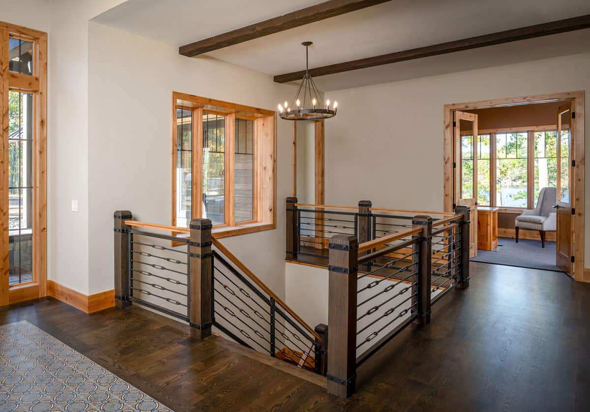Upstairs landing with iron stair railing, wood beam ceiling, and candle-style chandelier