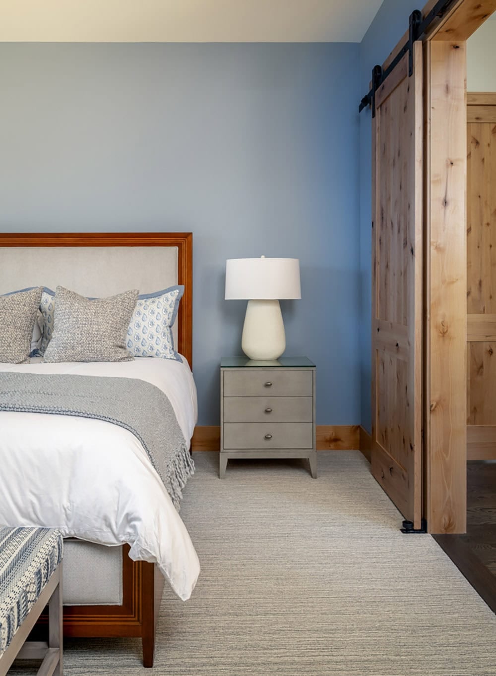 Bedroom corner with upholstered headboard, gray nightstand, and sliding barn door