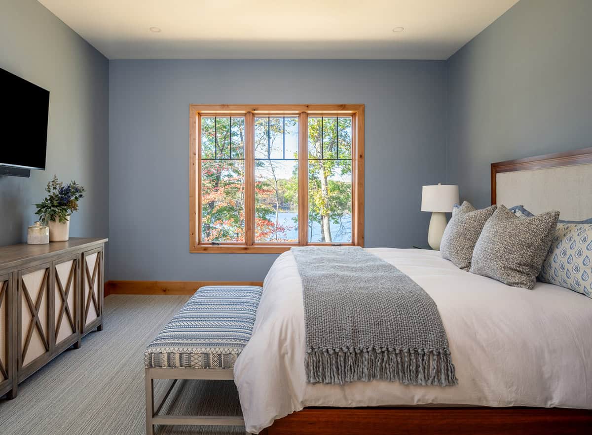 Blue-gray bedroom with wood-framed window showing lake view and wall-mounted TV