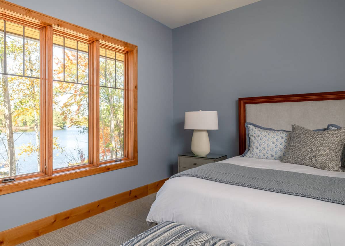 Bedroom with large wood-trimmed window overlooking the lake beside an upholstered headboard bed