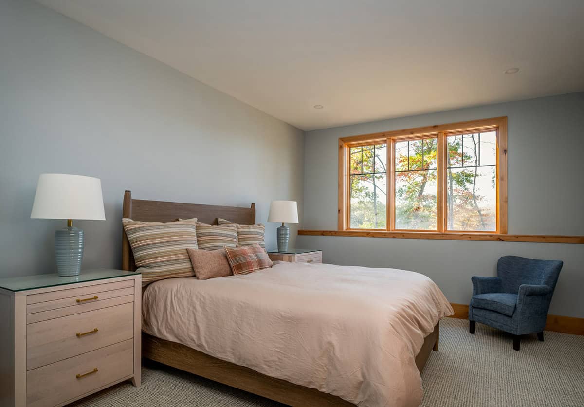 Guest bedroom with wood headboard, striped pillows, blue armchair, and triple window