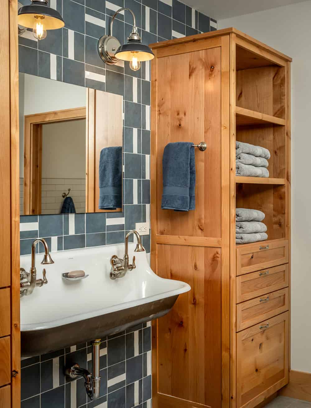 Bathroom with trough sink, patterned blue tile, and built-in wood linen cabinet with folded towels