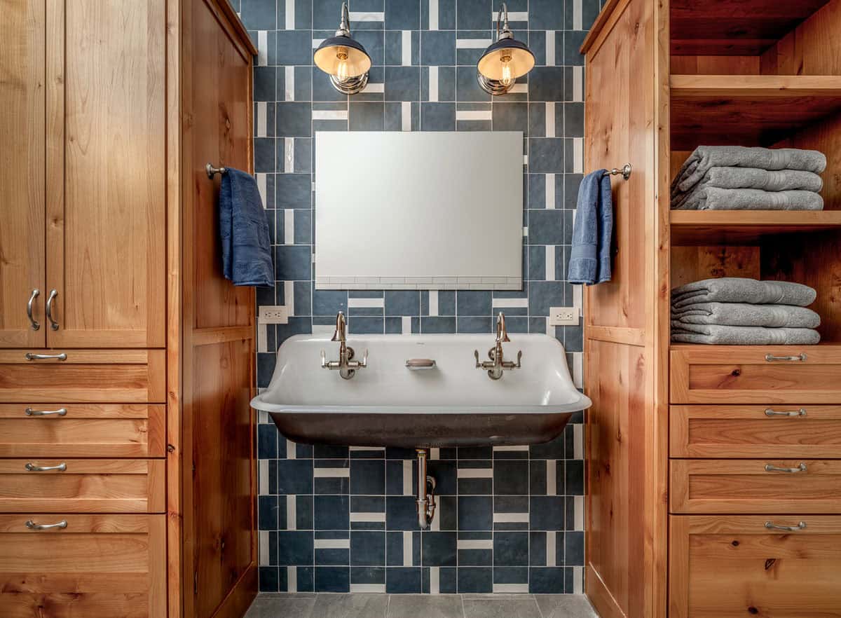 Symmetrical bathroom nook with cast-iron trough sink, patchwork tile, twin sconces, and wood cabinetry